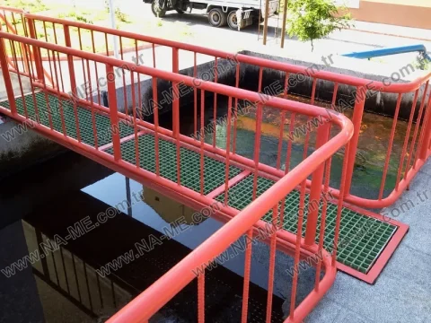 Red-railed grating walkway over a wastewater pool