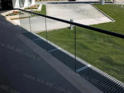 Linear grating under a glass railing in a landscaped area
